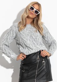 Szary sweter w warkocze z długimi rękawami, zestawiony z czarną skórzaną mini spódnicą z zamkami i kółkami. Na nosie kwadratowe białe okulary przeciwsłoneczne.