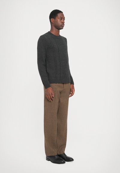 Pull en maille gris foncé avec un panneau avant texturé, associé à un pantalon à carreaux marron. Chaussures noires. Vue de côté.
