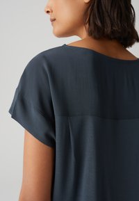 Top corto a maniche corte di colore blu scuro, con una texture morbida e scollatura a barca. Presenta una cucitura orizzontale sul retro e una vestibilità comoda.