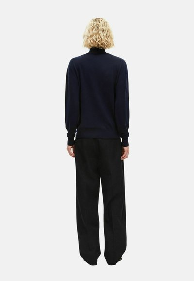 Jersey de cuello alto azul marino con puños y dobladillo acanalados, combinado con pantalones negros de cintura alta. Textura suave, diseño simple y corte relajado.