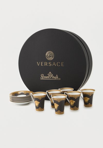 Σετ έξι μαύρων και χρυσών espresso φλυτζανιών Versace με αντίστοιχες πιατέλες, τοποθετημένα μπροστά από μια στρογγυλή κουτί με το λογότυπο Versace Rosenthal.
