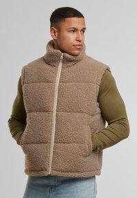 Beige színű fleece mellény magas gallérral, cipzáras záródással és két elülső zsebbel. A mellény puha, texturált felülettel rendelkezik és tűzött.