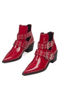 Botas de tobillo de charol rojo con punta afilada, tacones redondeados y dos correas con hebillas que presentan ojales de metal como detalle decorativo.