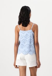 Top sem mangas azul claro com um design de olhais, bainha ondulada e alças finas, combinado com calções brancos. Material de algodão texturizado.