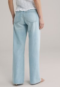 Jeans a gamba larga in denim azzurro chiaro con vita alta, dotati di doppie tasche posteriori e finitura pulita. Texture liscia con dettagli minimi.