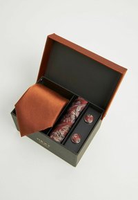 Cravate en satin marron avec pochette de costume à motif floral et boutons de manchette en argent, présentée dans une boîte noire avec un couvercle orange.