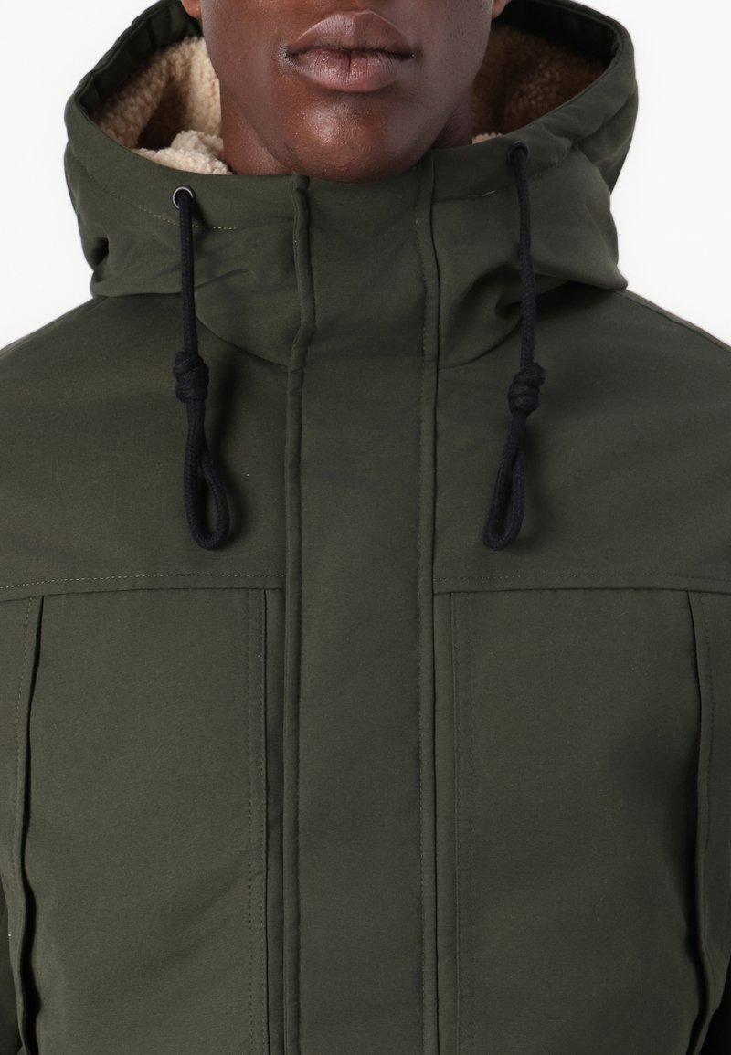 Veste à capuche verte avec une doublure beige texturée, dotée de deux poches avant et de cordons de serrage sur la capuche pour un ajustement.