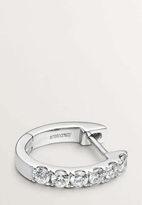 Pendiente de aro de plata con una superficie suave, que presenta una fila de cinco piedras de strass redondas y transparentes. Grabado con el nombre de la marca "aristocrazy."