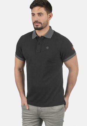 Zwarte poloshirt met grijze kraag en mouwboorden, voorzien van een klein logo op de borst en een leren patch op de arm. Van katoen.
