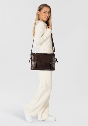 Bolso mensajero de cuero marrón oscuro con acentos de doble hebilla, asa superior, correa ajustable y dos bolsillos frontales. Textura suave, forma rectangular.