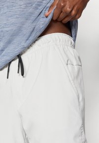 Ανοιχτό γκρι σορτς με ελαστική μέση και κορδόνι, που διαθέτουν πλαϊνές τσέπες και απαλή υφή. Μερική προβολή πάνω σε ουδέτερο φόντο.