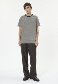 Dryžuota pilkai balta trumpomis rankovėmis marškinėliai su tamsiai mėlynu apvaliu kaklu, derinami su tamsiai rudos spalvos laisvo kirpimo kelnėmis ir juodais batais.