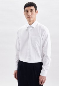 Camicia bianca a maniche lunghe con chiusura a bottoni, una tasca sul petto e colletto classico. Tessuto morbido con taglio su misura.