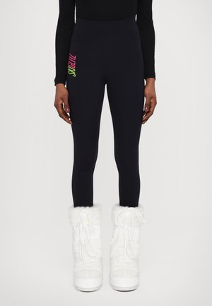 Black high-waisted leggings with a neon graphic on the side. Paired with white fur-lined winter boots. Smooth texture and fitted shape.
