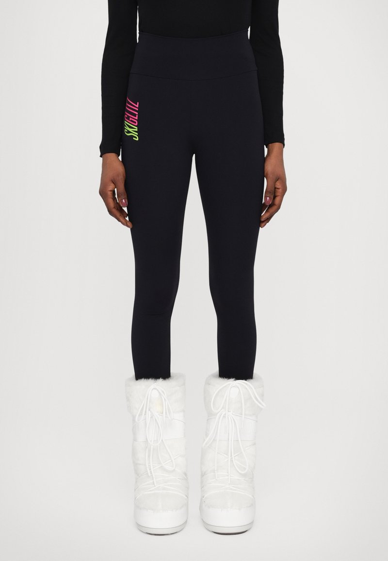 Fekete, magas derekú leggings, neon grafikával az oldalukon. Fehér, szőrmebéléses téli csizmával párosítva. Sima textúra és testhezálló fazon.