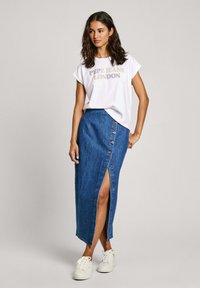 Bílé tričko s krátkým rukávem s potiskem "PEPE JEANS LONDON", spárované s džínovou sukní ke kolenům s knoflíky a bočním rozparkem. Bílé tenisky.