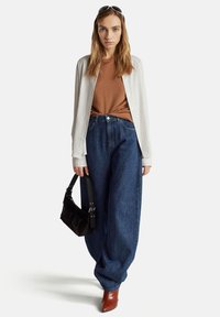 Licht gestreepte button-up shirt over een bruine aansluitende top, gecombineerd met losse donkerblauwe spijkerbroek en bruine puntige hakken. Zwarte handtas.