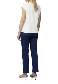 White short-sleeve top paired with dark blue jeans and silver high-heeled sandals. The top has a simple design with a smooth texture.