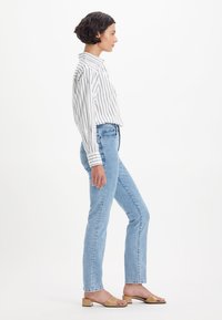 Prugasta srajca z dolgimi rokavi v beli in mornarsko modri barvi, v kombinaciji z svetloblujimi jeans hlačami ravne kroja in svetlo rjavimi natikači z blok peto.