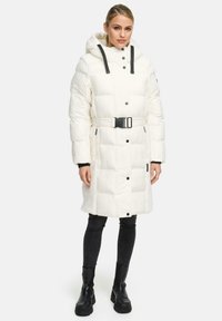 Witte gewatteerde jas met een capuchon, zwarte accenten, een riem en knoopsluitingen. Gestructureerde stof zichtbaar in het onderste gedeelte. Draag met zwarte jeans.