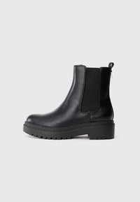 Stivale alla caviglia in pelle nera con suola spessa, pannelli laterali elastici e linguetta sul retro, mostrato in profilo su uno sfondo bianco.