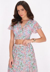Blumen-Crop-Top und passender Rock in Hellblau mit pinken Blumen. Das Material ist durchsichtig, mit fließenden Ärmeln und einer taillierten Passform.