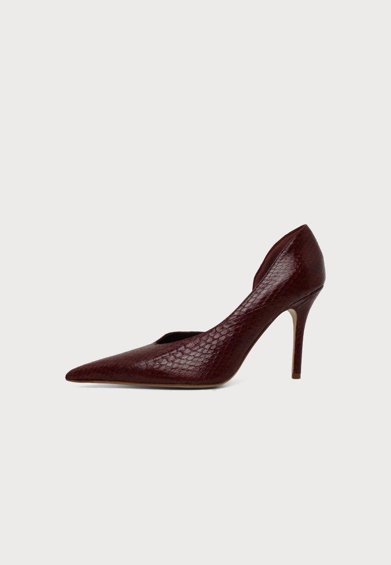 Chaussure à talon haut rouge foncé avec bout pointu et motif texturé ressemblant à de la peau de serpent, vue de profil sur un fond clair.