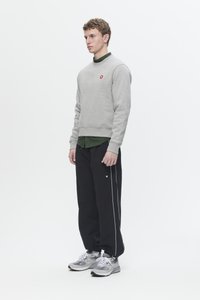Gray sweatshirt with red logo, green striped shirt underneath, black pants with white side stripes, and gray sneakers, standing model.