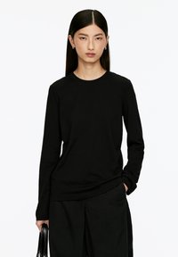 Schwarzes Langarm-T-Shirt aus Baumwolle mit runder Ausschnitt, lockerer Passform und weicher Textur; kombiniert mit schwarzen weit geschnittenen Hosen.