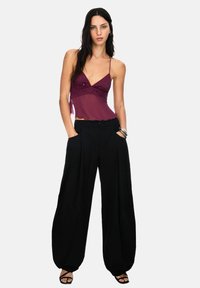 Bourgogne silke cami-top med broderad design, tillsammans med löst sittande, högmidjade svarta byxor och svarta sandaler med remmar.
