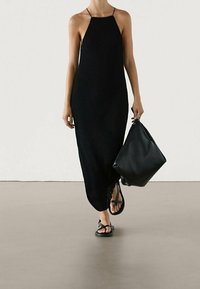 Mustikka ribbed neulemaksi mekko ohuiden hihnojen kanssa, jossa on sivuaukko. Yhdistetty mustiin litteisiin sandaaleihin ja suureen mustaan olkalaukkuun.