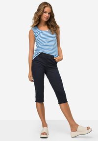 Un débardeur rayé bleu associé à un pantalon cropped marine foncé et des sandales à plateforme beiges, montrant une coupe décontractée et un design casual.