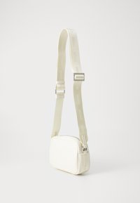 White rectangular sling bag made of smooth material. Features a branded strap and silver hardware, with a zip closure on the top.