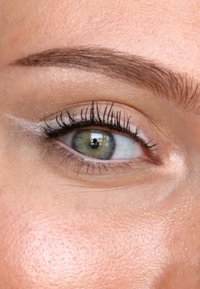 Närbild av ett grönt öga med mörka ögonfransar, lätt smink och en slät, lysande hudstruktur som visar subtila rosa undertoner runt ögat.