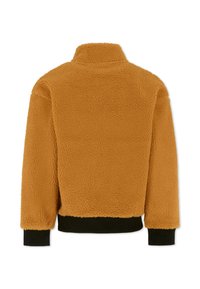 Veste en fausse fourrure d'un jaune moutarde chaud, avec un col haut et des poignets en maille noire au niveau de l'ourlet et des manches. Fini doux et texturé.