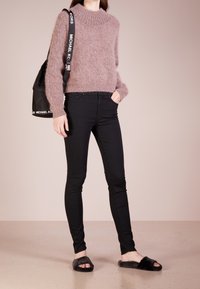 Ljust lila fluffig tröja, svarta slim fit-jeans och svarta fuskpäls-tofflor. Svart väska med "MICHAEL KORS"-rem i detalj.