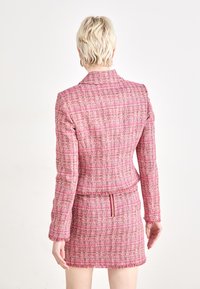 Vaaleanpunainen tweed-takki, jossa on samanvärinen minihame, joka sisältää tekstuuripatternin, fringed-reunat ja piilotetun vetoketjun takana.