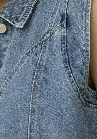 Džínová vesta světle modré barvy s límcem, zdobená kontrastním prošíváním a předním zapínáním na druky.