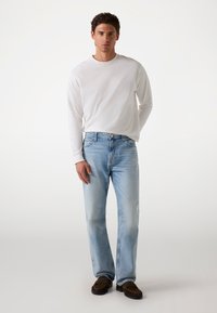 Jeans de mezclilla azul claro con un corte recto, combinados con una camiseta de manga larga blanca. El material parece suave con un ligero desgaste.