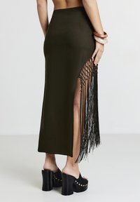 Gonna maxi verde oliva con spacco laterale e dettagli di frange nere. Abbinata a zeppe nere spesse con borchie dorate.