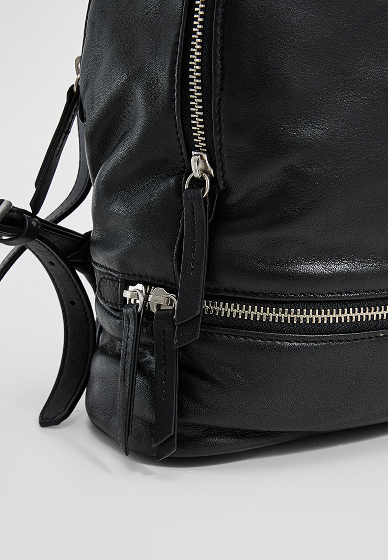 Schwarzer Leder-Rucksack mit glatter Textur, silberner Reißverschlussbeschläge und verstellbaren Trägern, versehen mit Akzentnähten und Reißverschluss-Anhängern.