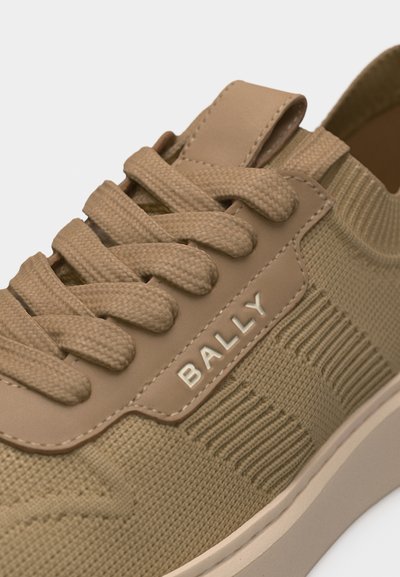 Gros plan sur une chaussure de sport beige en tricot avec de gros lacets et le logo "BALLY" sur la partie latérale en cuir.