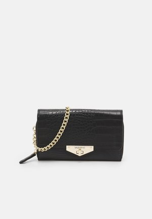 Czarna kopertówka z tłoczonej skóry krokodyla z złotym łańcuszkiem i złotym zapięciem Valentino, na jednolitym jasnym tle.