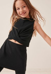 Schwarzes cropped Top aus strukturiertem Material mit einem Drehdesign, kombiniert mit einem schwarzen Minirock. Glatte Textur, schlichte Designelemente.