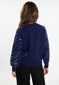 Navyblauer Strickpullover mit geripptem Saum und Bündchen; hat für zusätzliche Details Pailletten-Wellenmuster auf den Ärmeln.