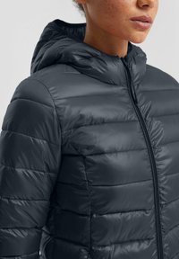 Tamno siva podstavljena jakna s kapuljačom, s patentnim zatvaračem sprijeda, kviltanom teksturom i prilagođenim dizajnom. Glatki, sjajni materijal.