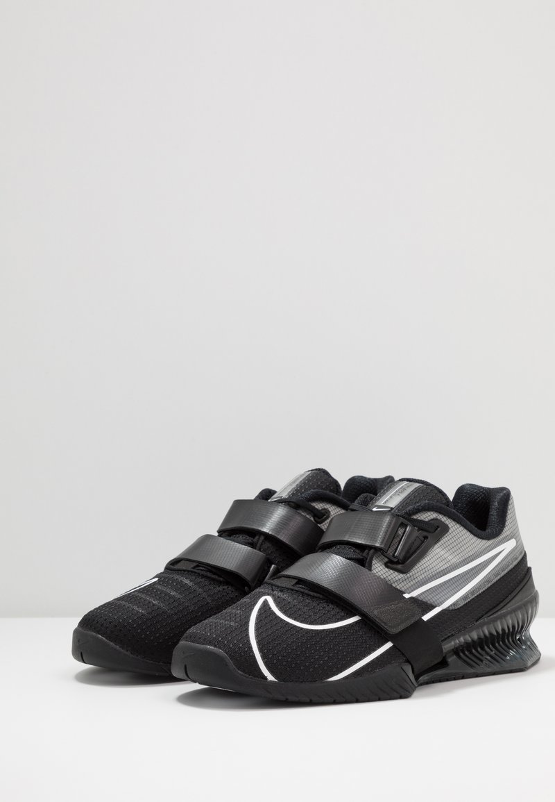 Czarne sportowe buty z teksturowaną siateczką, podwójnymi paskami rzepowymi, odblaskowymi akcentami oraz zakrzywioną podeszwą dla lepszej przyczepności.