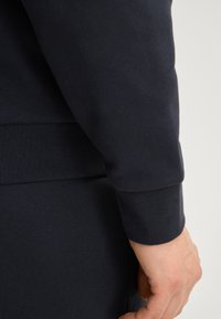 Felpa in cotone blu navy con polsini a costine, che presenta una texture liscia e un design aderente. La manica si estende fino al polso, integrandosi perfettamente con il corpo.