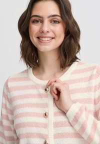 Svītrainā kardigāna ar gaiši rozā un krēmkrāsas tonim, izgatavots no adīta auduma, ar apaļu kakla izgriezumu un zelta pogu akcentiem.