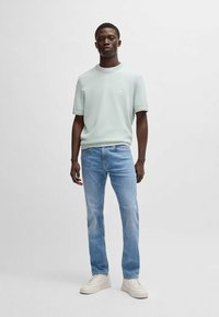 Ljusgrön, kortärmad tröja med ribbat nackband, bärs med ljusblå jeans. Har en liten logotyp på bröstet och enkla sneakers.